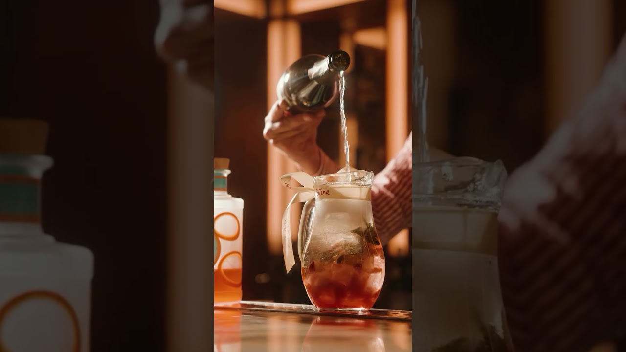 Cinematic close-up of a drink being poured over ice in warm amber light at a restaurant